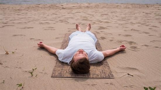 Illustrasjonsfoto av en mann som ligger på ei matte på stranda og praktiserer yoga nidra. 