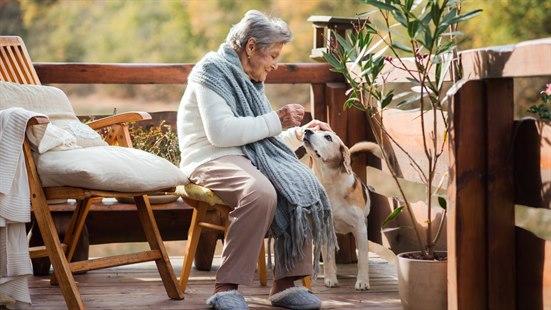 Eldre dame som sitter på en stol på verandaen sammen med hunden sin.
