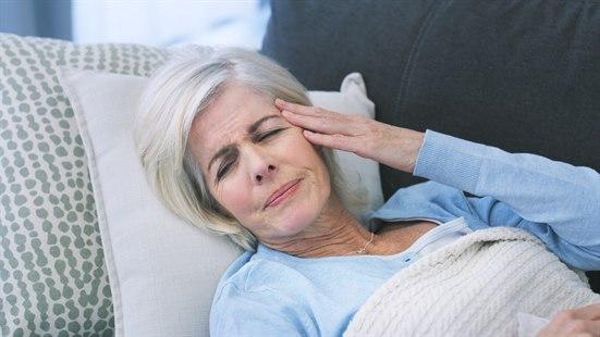 Illustrasjonsfotoet viser en eldre kvinner som ligger på sofaen og tar seg til venstre tinning