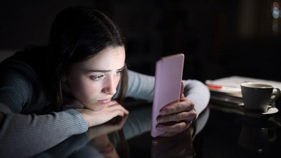 Illustrasjonsfoto: Unge jente ligger lent over et bord i et mørkt rom og ser på smarttelefonen sin.