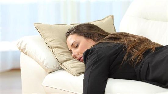 Fotoet viser overkroppen og ansiktet til en ung dame i svart dressjakke som ligger på magen på en sofa. Øynene er lukket, og hun ser sliten ut. 