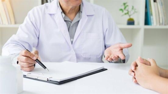 Illustrasjonsfotoet viser overkroppen til en lege som holder en penn over en notatblokk