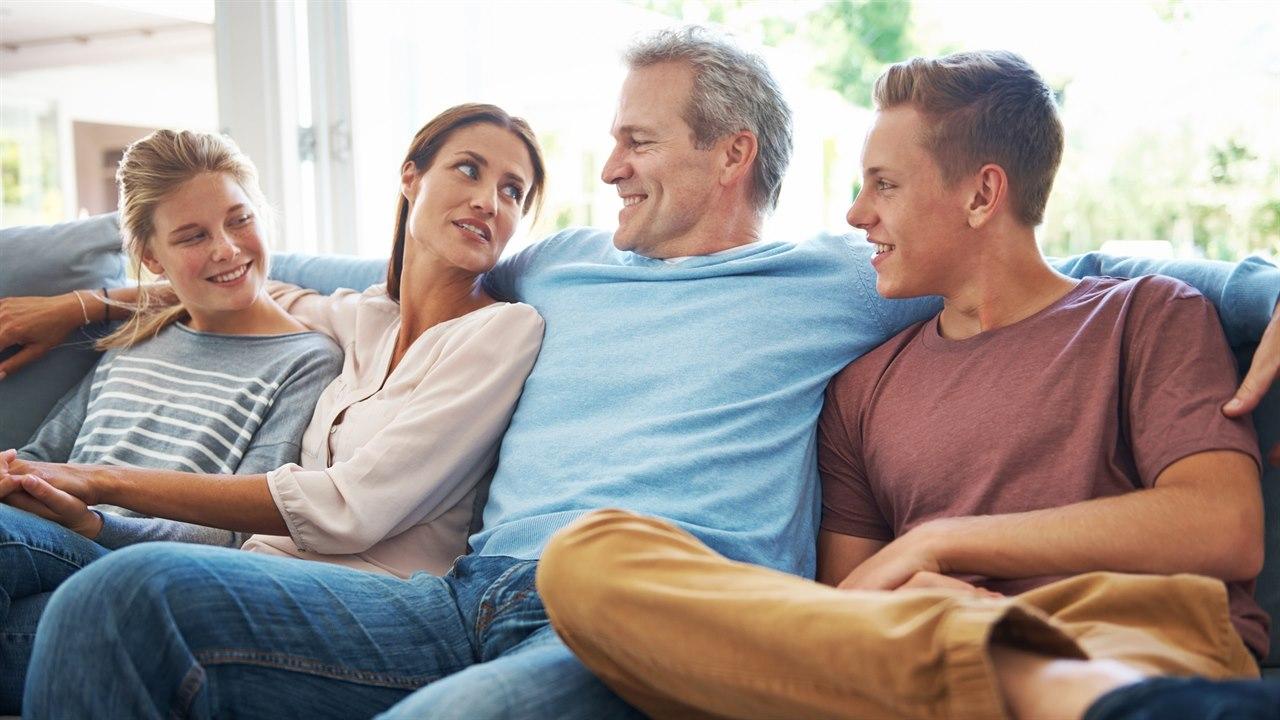 Illustrasjonsfotoet viser en familie som sitter i en sofa sammen. Fra venstre: Datter, mot, far og sønn. De ser mot hverandre og har det hyggelig.