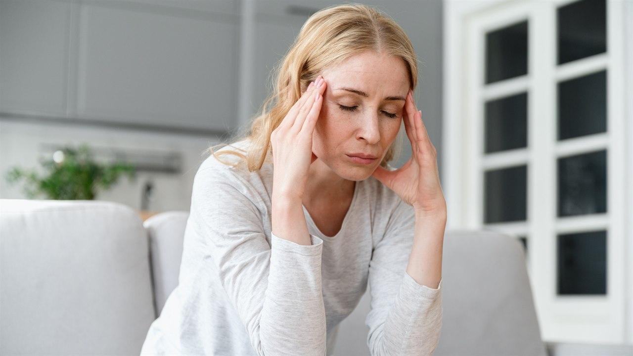 Illustrasjonsfotoet viser en kvinne som sitter i sofaen. Hun har smerter i bihulene, og trykker begge hendene sine mot ansiktet.
