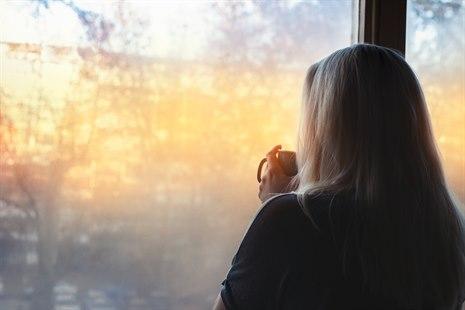 Illustrasjonsfot av en kvinne som vises bakfra og som står og ser ut av et vindu,