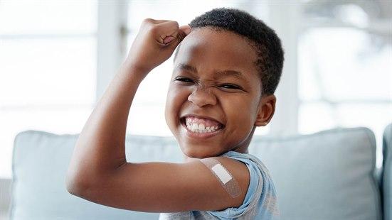 Illustrasjonsfoto av et afrikansk barn som smiler bredt etter å ha tatt vaksine. Barnet viser frem armmuskelen, og vi kan se plaster på overarmen.