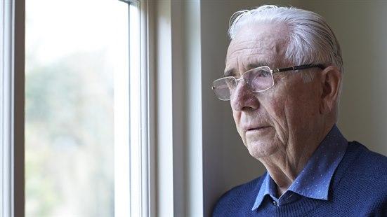 Illustrasjonsfotoet viser en eldre mann med briller som ser ut vinduet