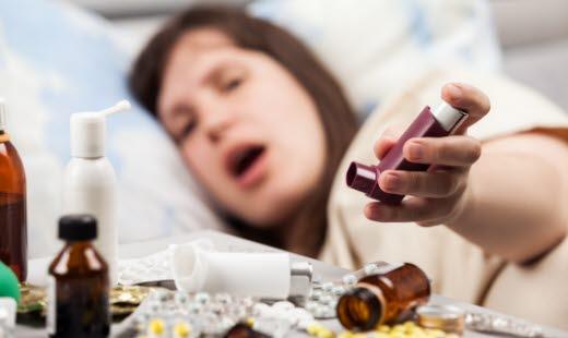 Illustrasjonsfoto av en dame som ligger med astmaanfall. Hun strekker armen mot inhalatoren.