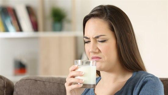 Illustrasjonsfoto: Kvinne holder et glass melk opp mot munnen og skjærer en grimase.