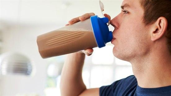 Illustrasjonsfotoet viser en mann med blå t-skjorte i profil. Han drikker brun drikke av en proteinshakeblender i plast.
