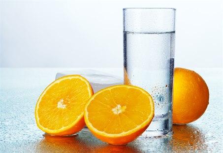 Illustrasjonsfoto av appelsiner og et glass vann på et bord.