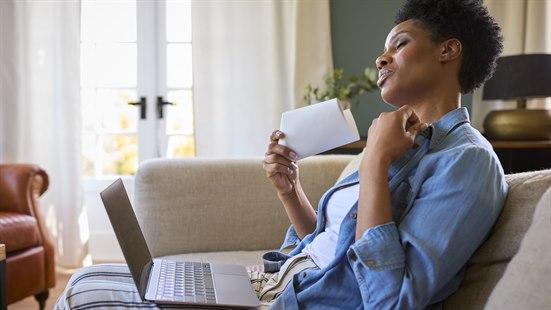 Illustrasjonsfoto av kvinne som sitter i en sofa med pc i fanget og bruker et papir som vifte.