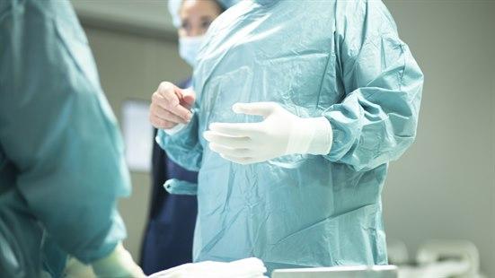 Illustrasjonsfotoet viser en kirurg som er kledd i grønn frakk og som er i ferd med å ta på seg en engangshanske