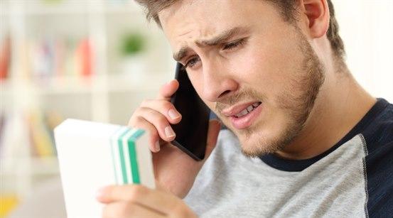 Bekymret ung mann som leser pakningsvedlegg på medisin mens han snakker i telefon.
