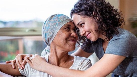 Illustrasjonsfotoet viser to kvinner i en sofa, der den ene er alvorlig syk. Venninnen holder rundt henne, og blikket viser kjærlighet og støtte.