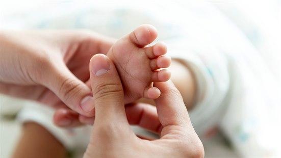 En voksen undersøker foten til en nyfødt baby.