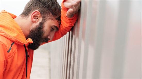 Mann i oransje treningsjakke er sliten og lener hodet mot veggen