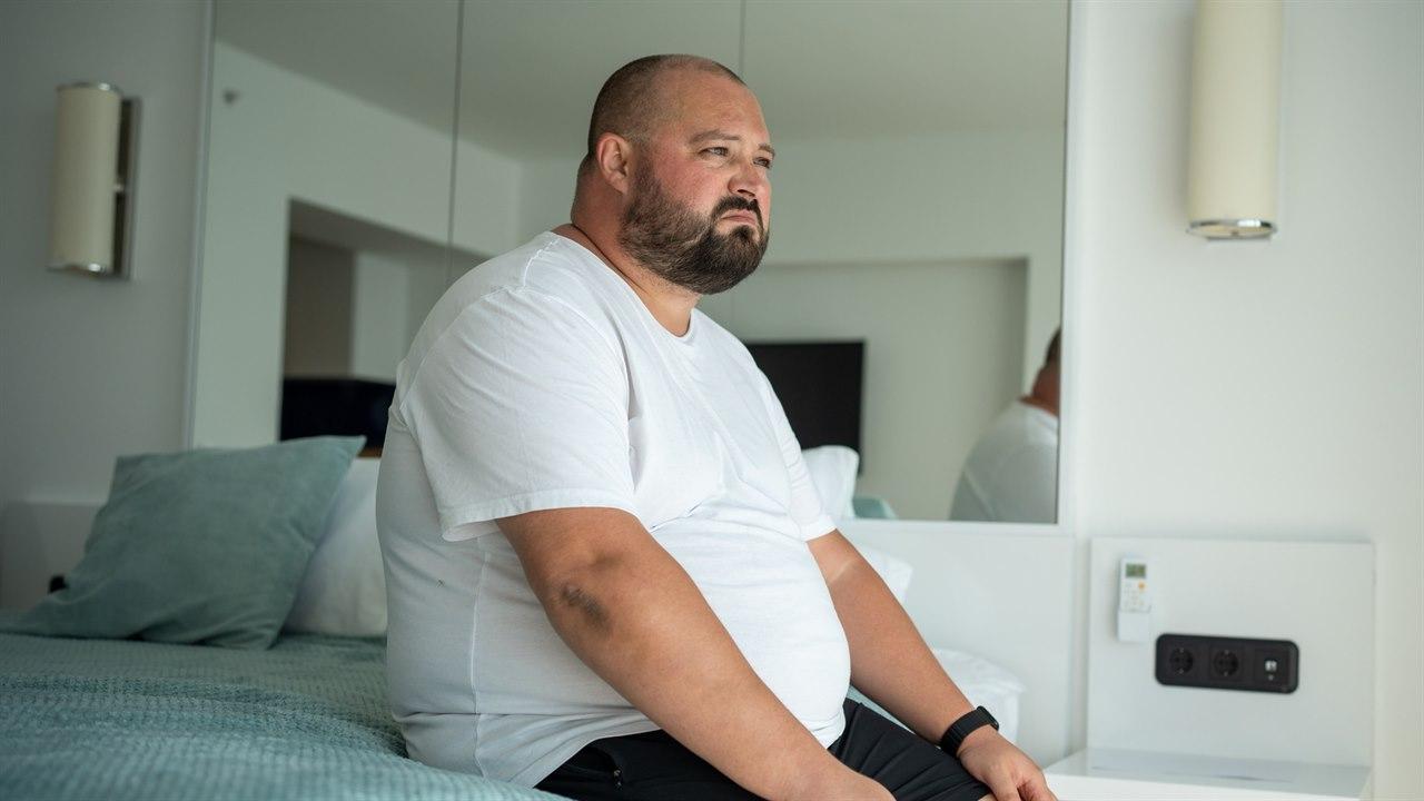 Illustrasjonsbilde viser en overvektig mann i 40-årene som sitter på sengen sin og ser utover rommet. 