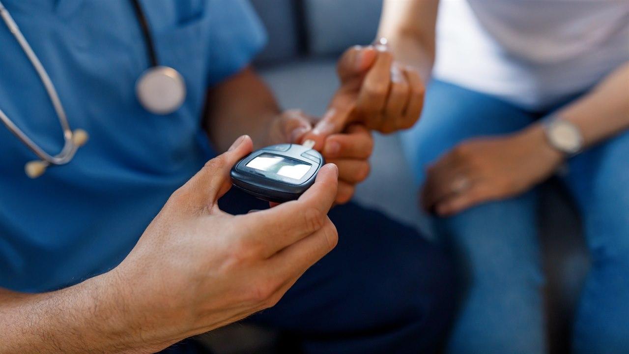 Illustrasjonsbilde viser en lege som måler glukosen for sjekke en pasient med diabetes. Det er fokus i bilde på hånden til legen som stikker i fingeren til pasienten. 