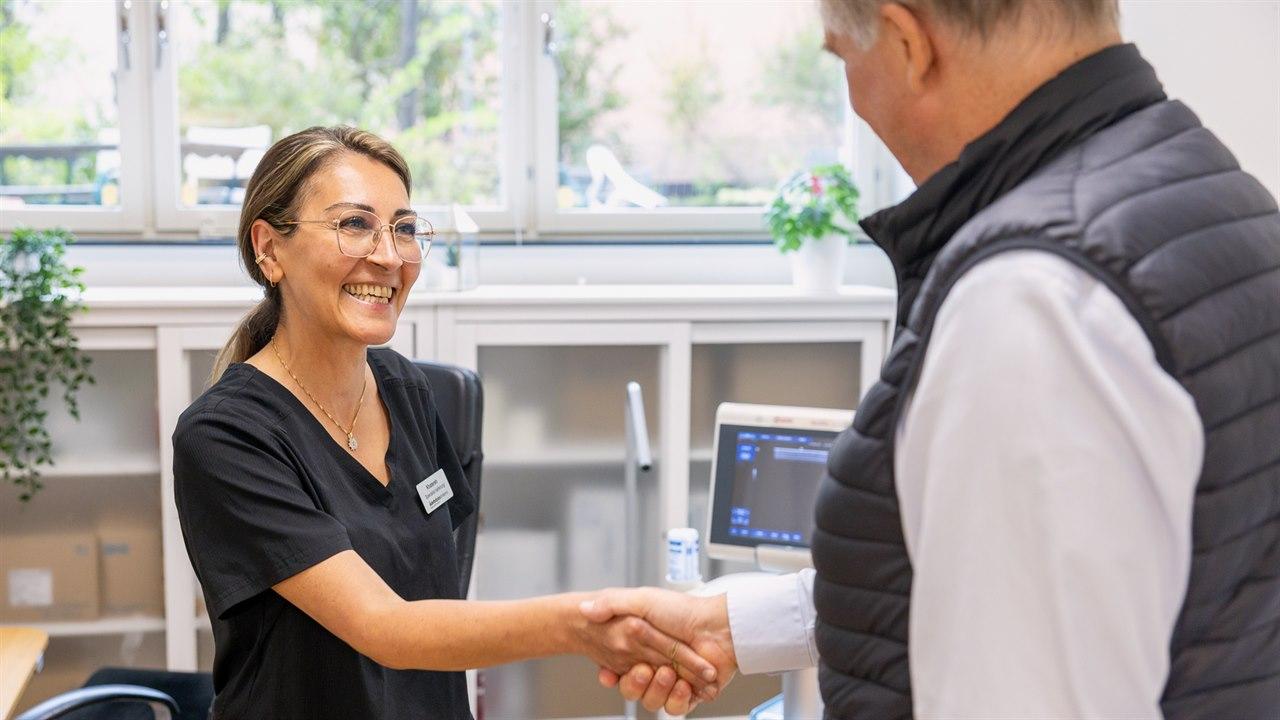Illustrasjonsfotoet viser en mann som hilser på en smilende kvinnelig ansatt hos Åreknutklinikken.