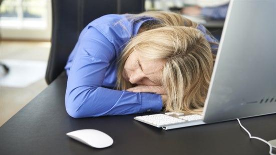 Middelaldrende kvinne som tar seg en høneblund foran datamaskinen.