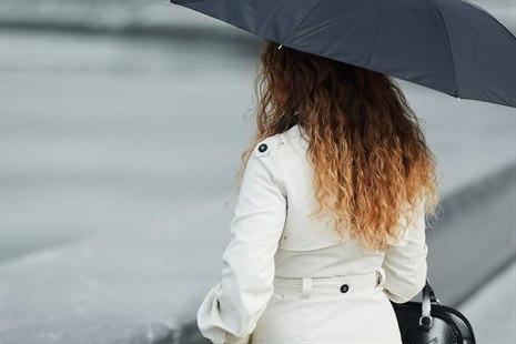 Vi ser en kvinne med paraply som ser ut mot vannkanalen. Hun er vendt fra oss.