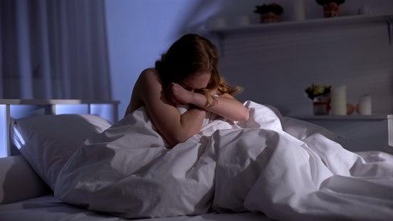 Ung kvinne som sitter oppreist i seng på natten, tydlig skremt eller plaget av minner.