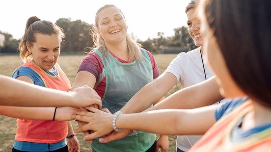 Illustrasjonsbildet viser en gruppe kvinner som er utendørs og trener. De står i ring med hendene i midten for heiarop.