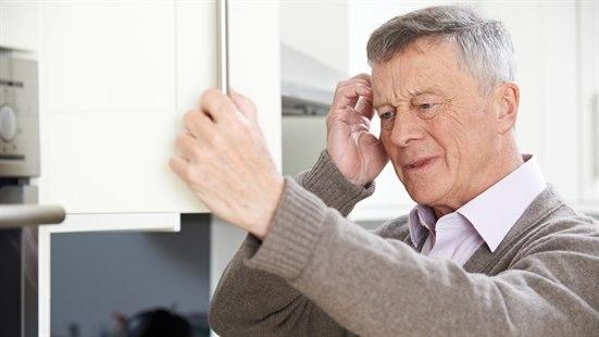 Fotoet viser armene og ansiktet til en eldre mann som åpner et skap på kjøkkenet. Han tar seg på hodet med den ene hånden og har et ansiktsuttrykk som om han prøver å huske noe.