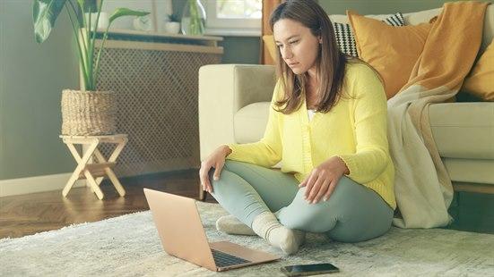 Illustrasjonsfotoet viser en kvinne som sitter på et teppe foran en laptop