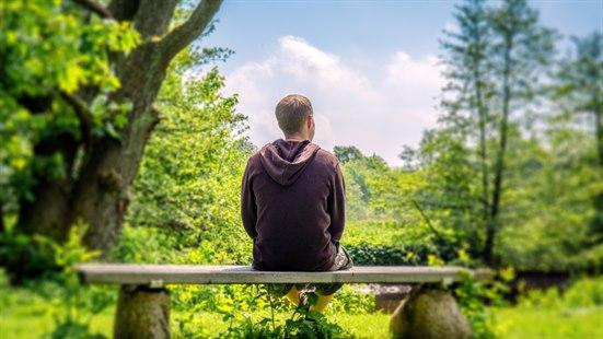 Illustrasjonsfoto av en mann som sitter med ryggen til på en benk i grønn natur.