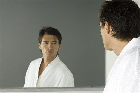 Illustrasjonsfoto viser en mann i morgenkåpe. han ser på seg selv i speilet med et alvorlig uttrykk.